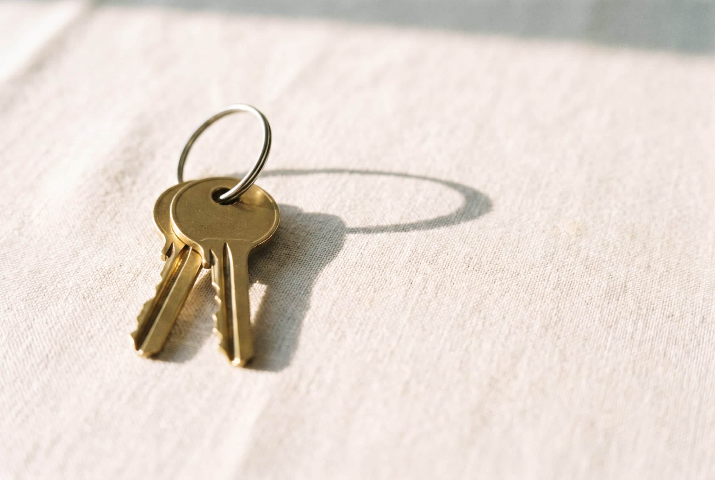 Two house keys on a ring, resting on pale linen in bright daylight.