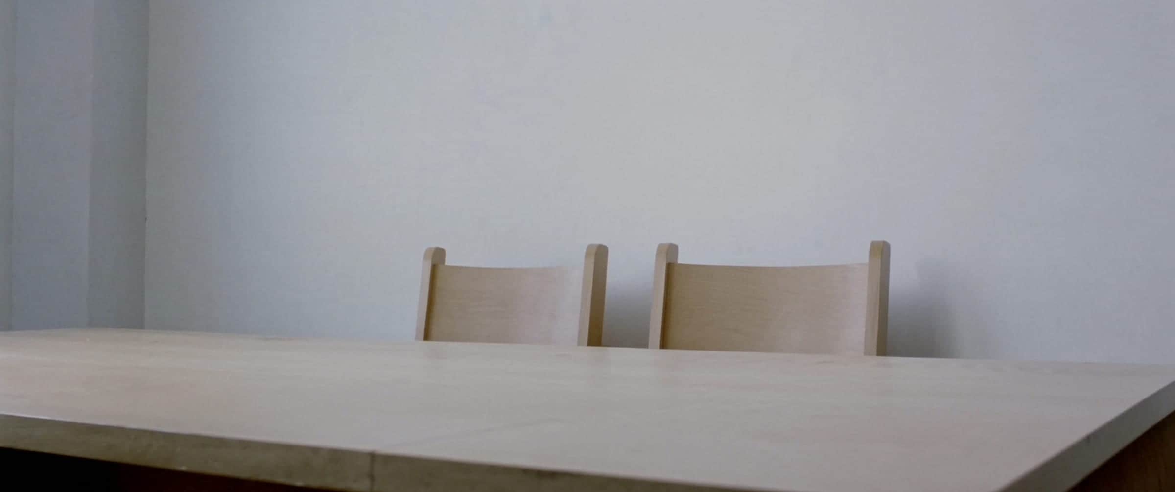 An empty meeting room, two plain wooden chairs at a pale table under even daylight.